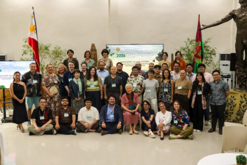 A group photo of approximately 50 participants of the 2026 Island Studies International Conference (ISIC) gathered inside the Leyte Samar Heritage Center in Tacloban City. The Philippine and UP flags are visible on either side of the group, with the iconic statue inside the venue partially seen on the right. The participants, wearing conference name tags, smile toward the camera at the conclusion of the three-day international conference.